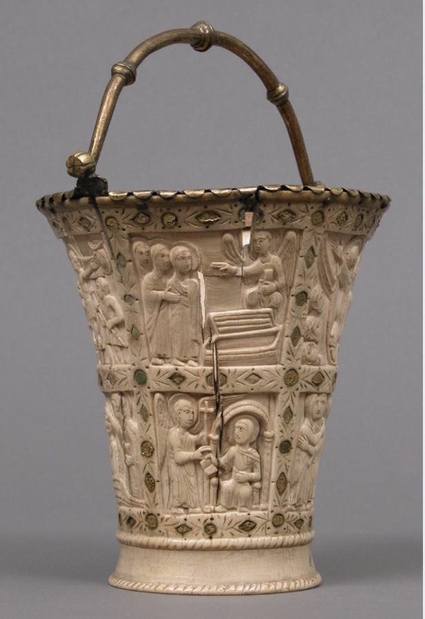Photo of a bucket-like object that depicts religious scenes on sides with handle on top.