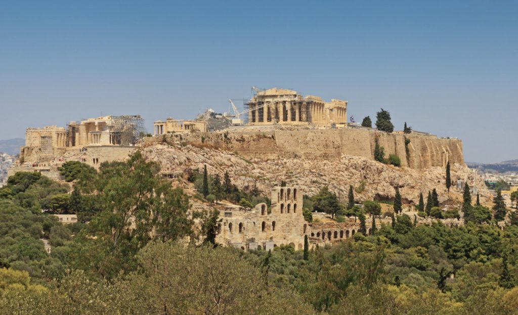 Photo of the Acropolis on the top of a hill with decrepit structures surrounding it.