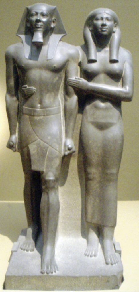 Photo of Egyptian pharaoh and queen standing with erect posture in traditional dress.