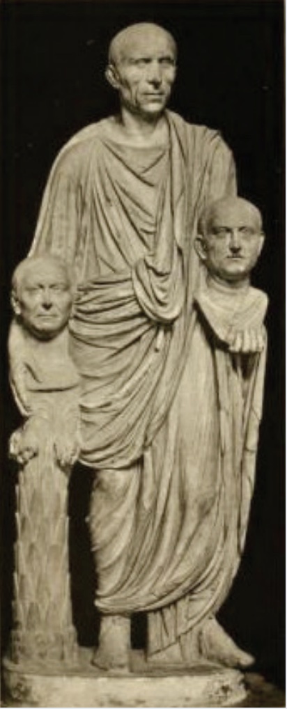 Photo of sculpture of robed and bald man holding busts of other men in each hand.